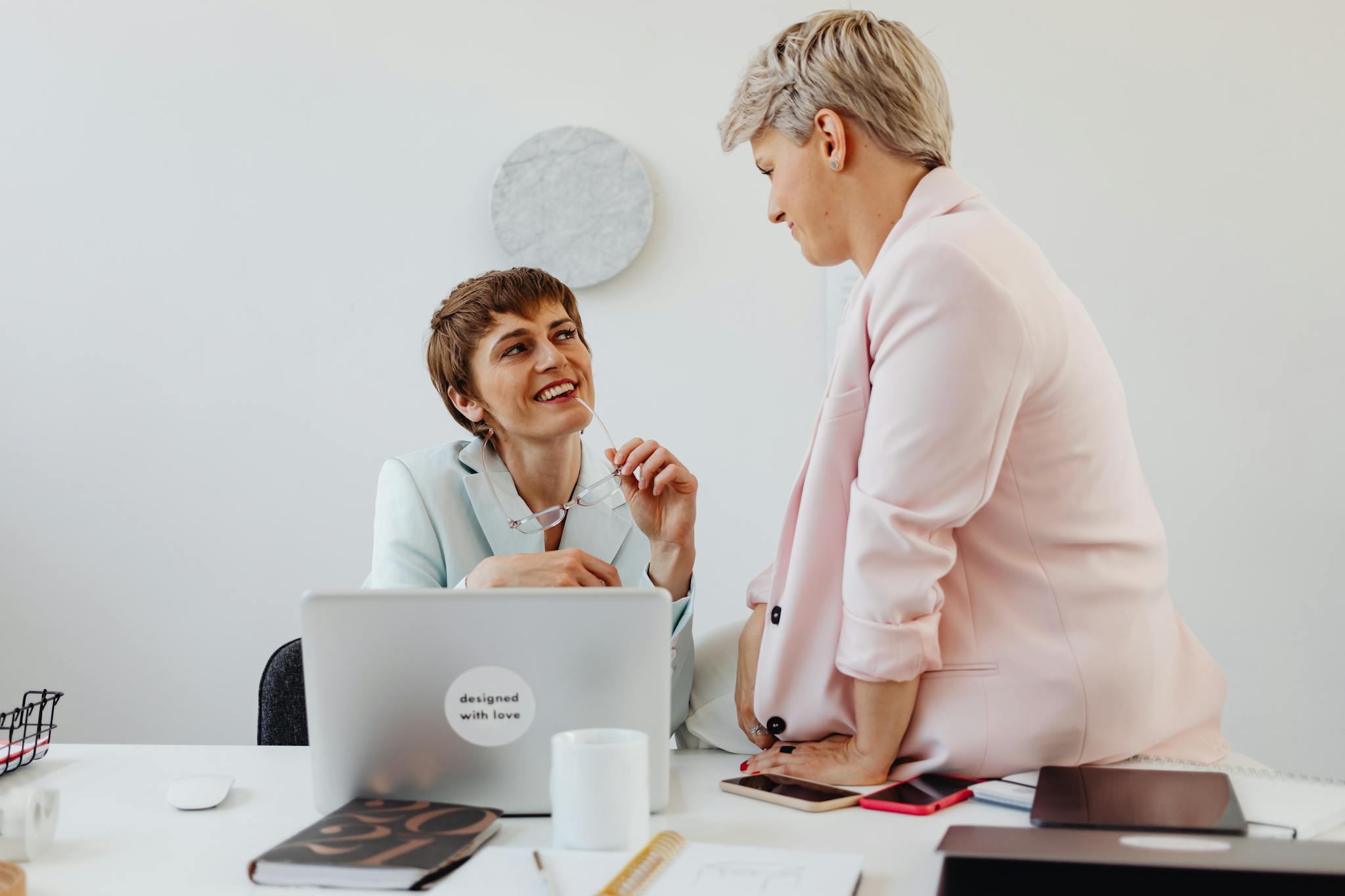 Two professional women interact warmly in an office, promoting teamwork and connection.